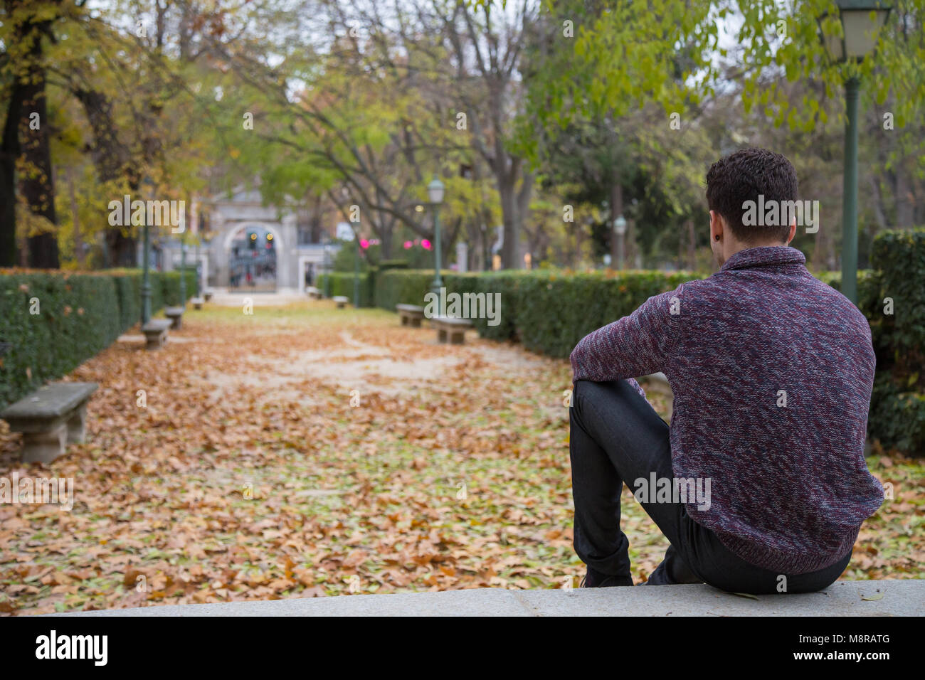 Thoughtful young man sitting on stairs in autumn park and looking away ...