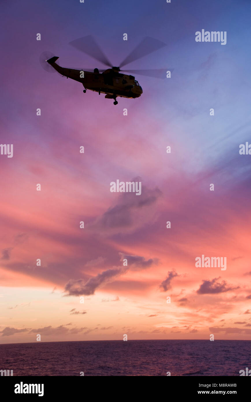 Silhouette of helicopter flying into sunset Stock Photo