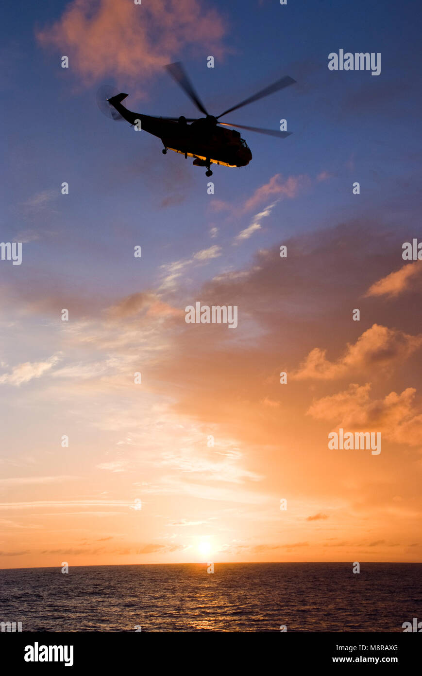 Silhouette of helicopter flying into sunset Stock Photo