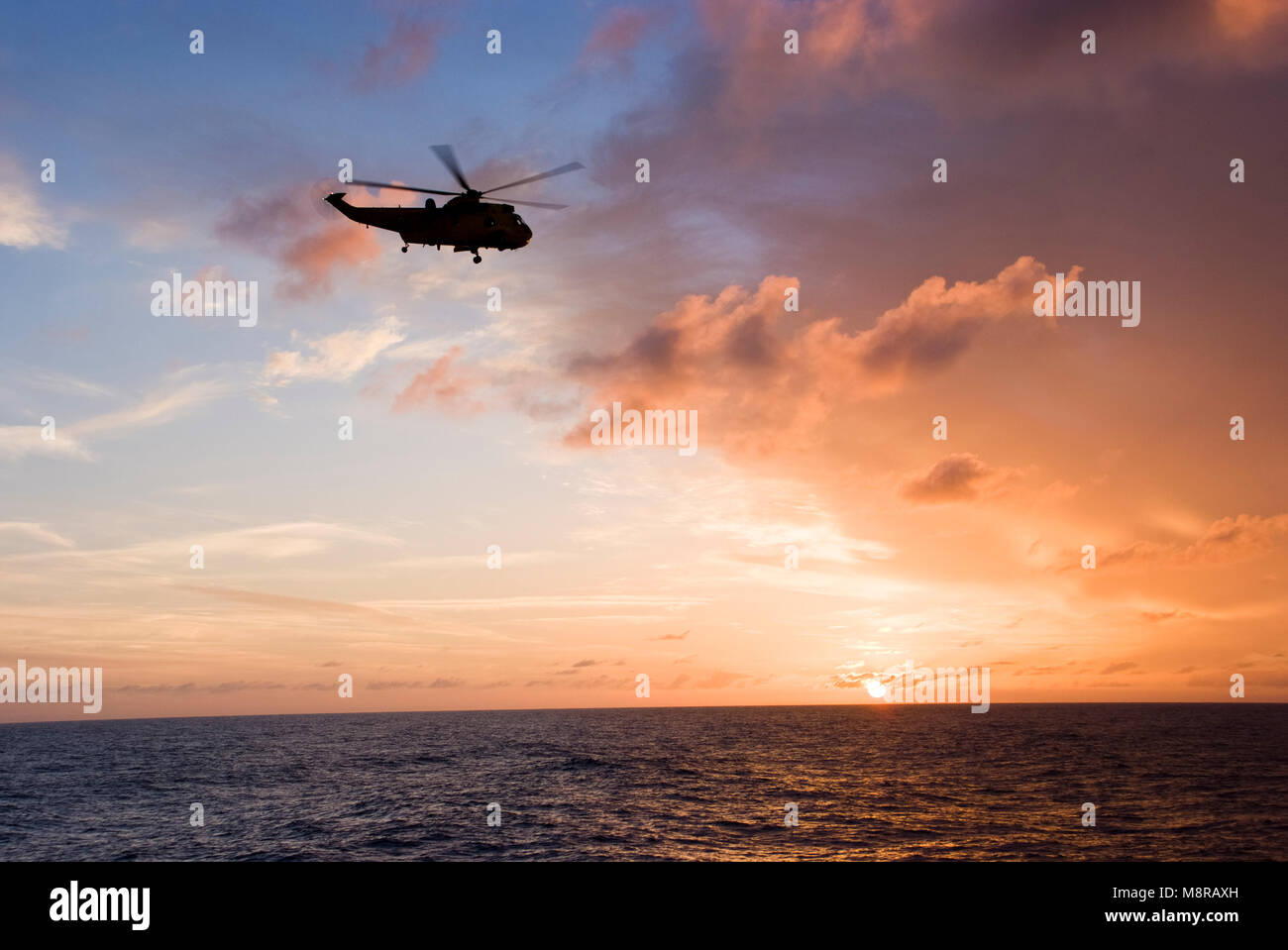 Silhouette of helicopter flying into sunset Stock Photo
