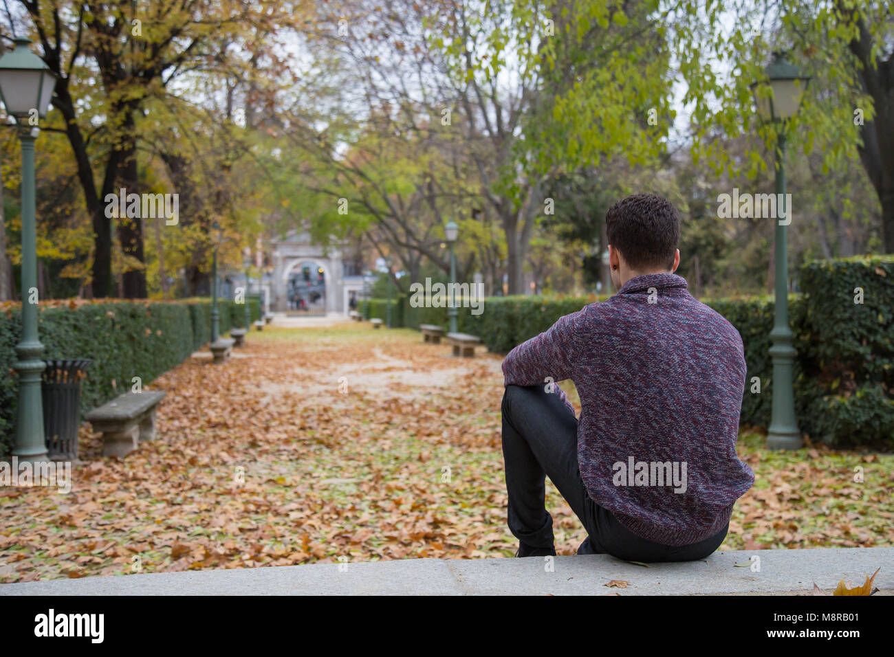 Thoughtful young man sitting on stairs in autumn park and looking away ...