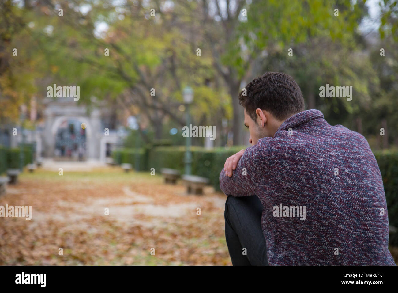 Thoughtful young man sitting on stairs in autumn park and looking away ...