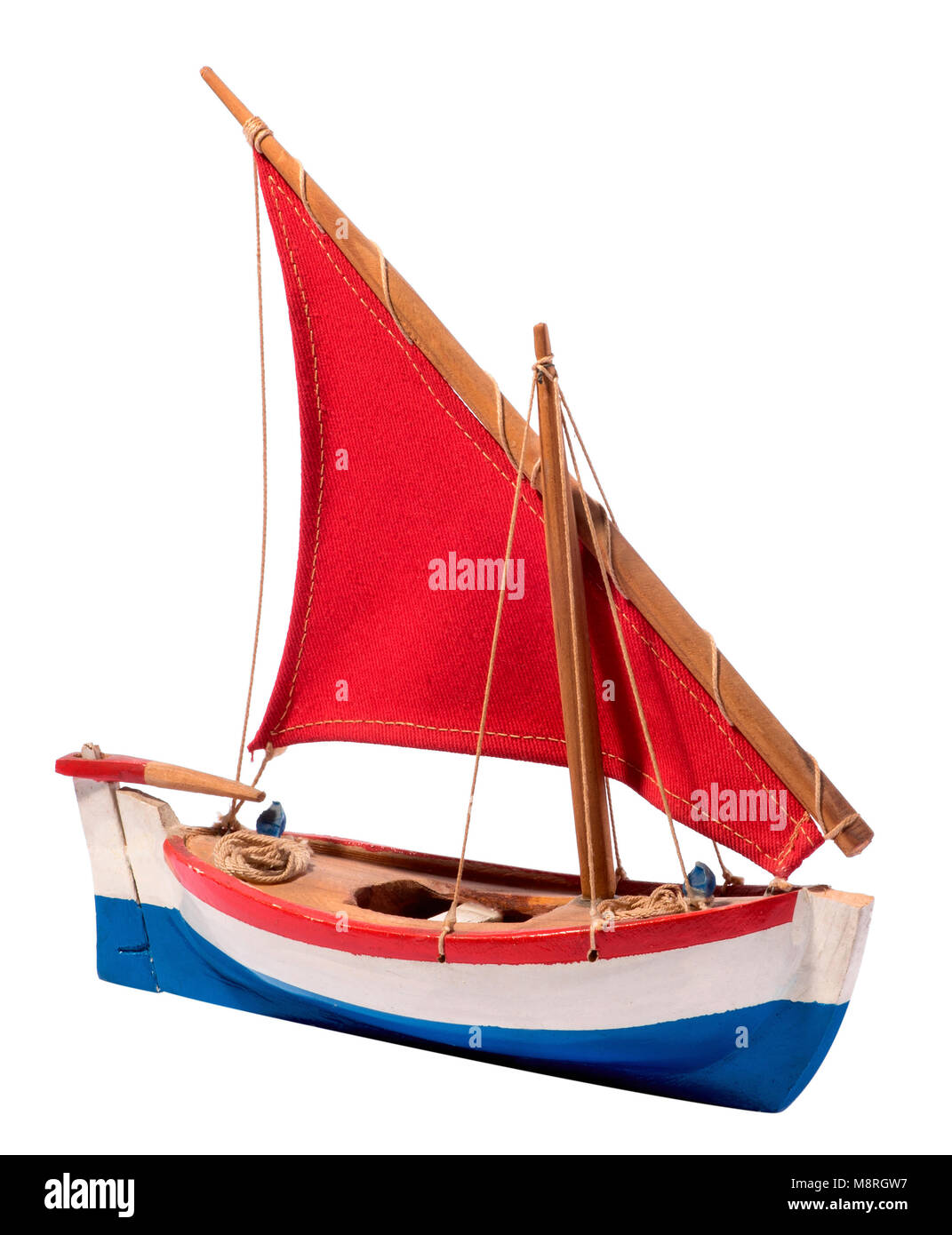 Colorful simple wooden handcrafted sailing boat with red sail and red, white and blue colors on the hull and a rudder and tiller isolated on white Stock Photo