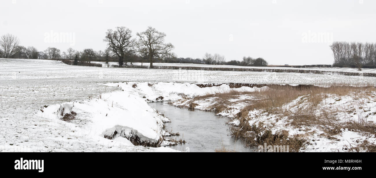 An image of a stream flowing through a snow covered field in early spring at Newton Harcourt, Leicestershire, England, UK Stock Photo