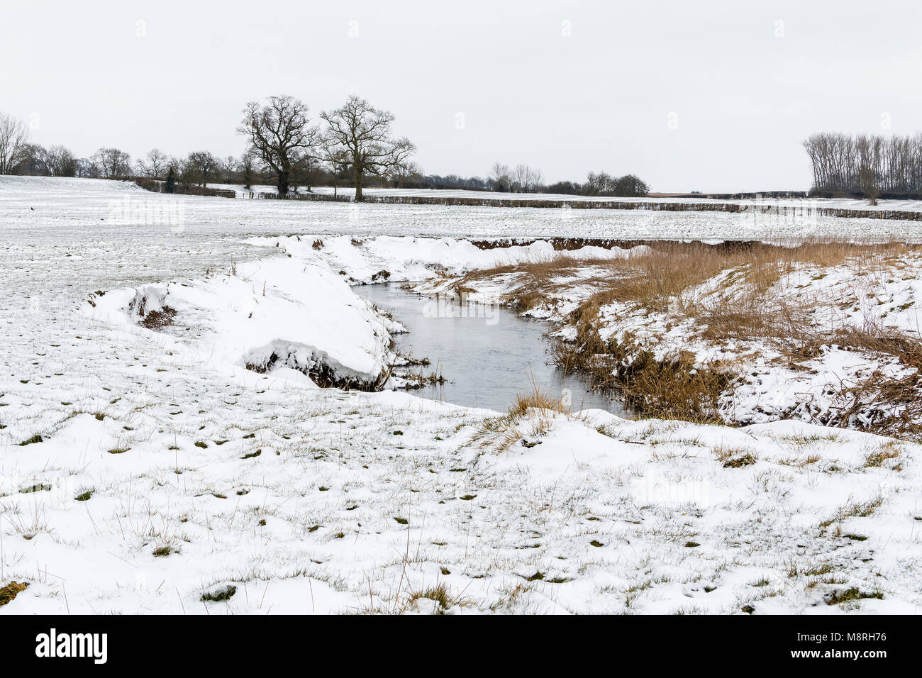 An image taken on a cold spring morning showing a stream and snow covered fields at Newton Harcourt, Leicestershire, England, UK Stock Photo