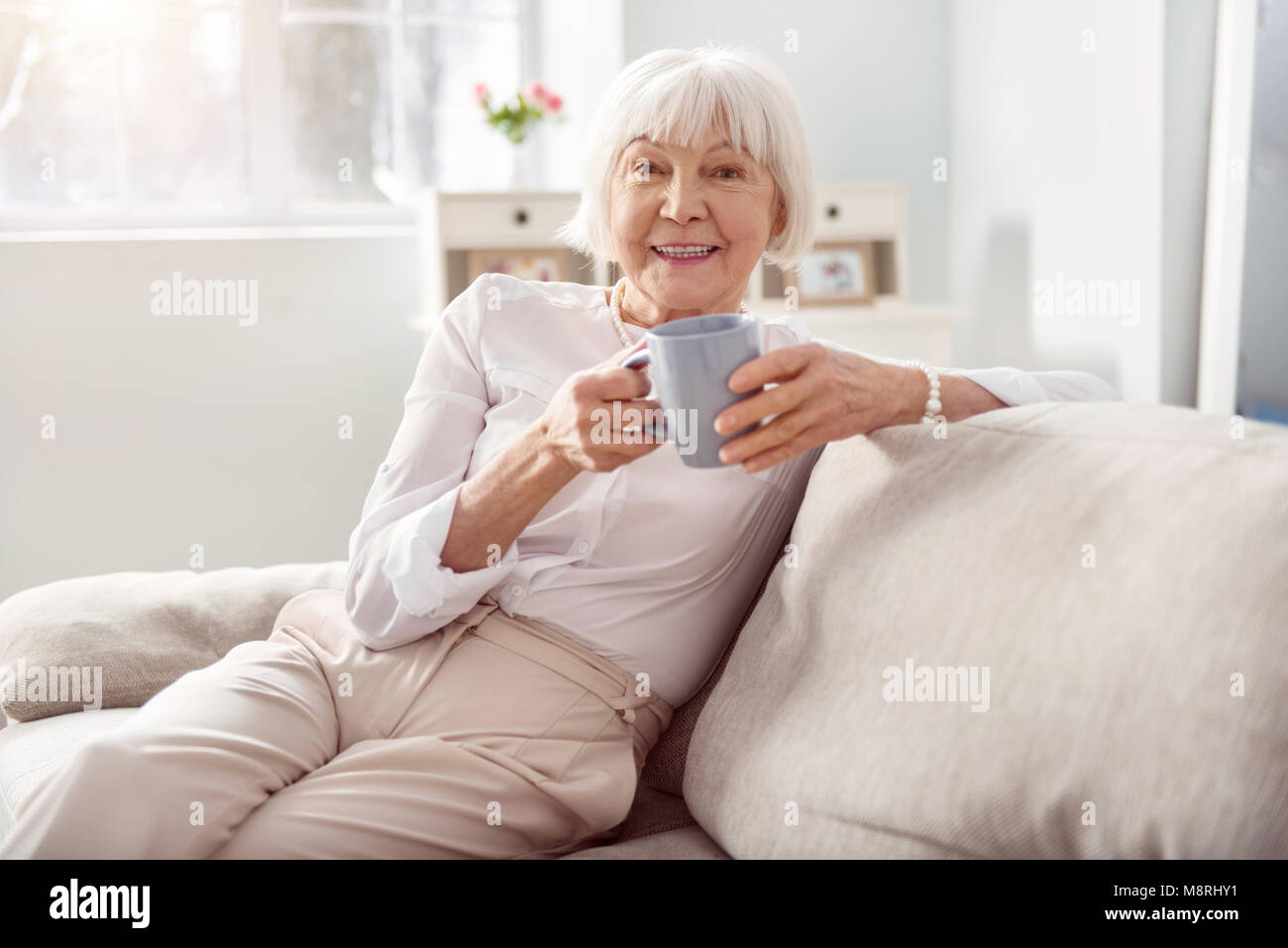 Upbeat senior woman drinking coffee on sofa Stock Photo