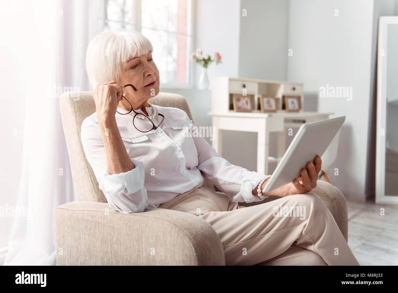 Charming elderly lady reading from tablet attentively Stock Photo