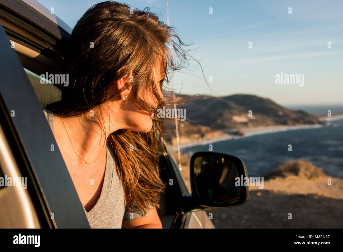 Woman looking through car window at beach against sky during sunset Stock Photo