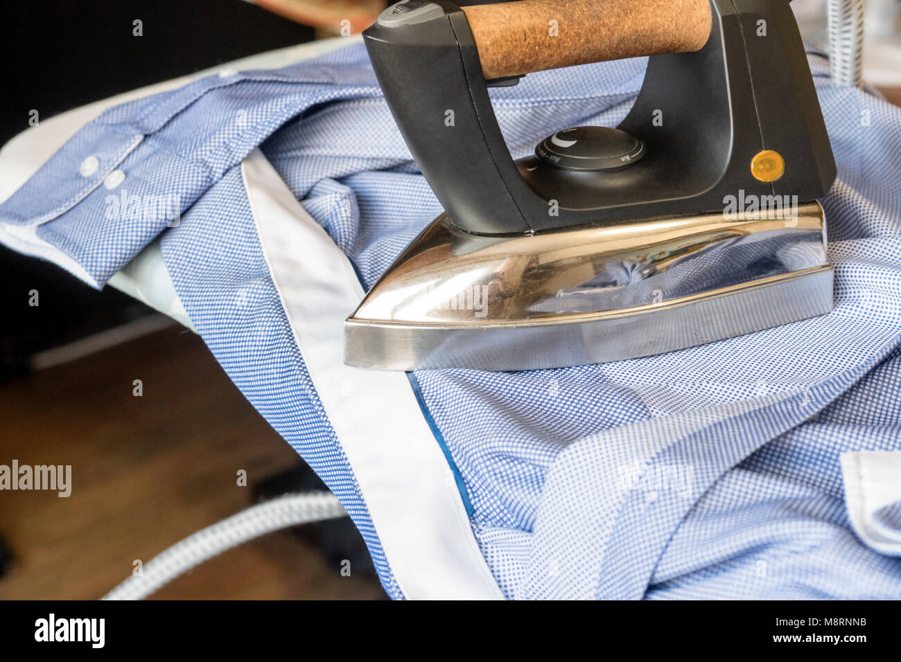 The iron strokes the man's blue shirt. Cleanliness and tidiness Stock Photo