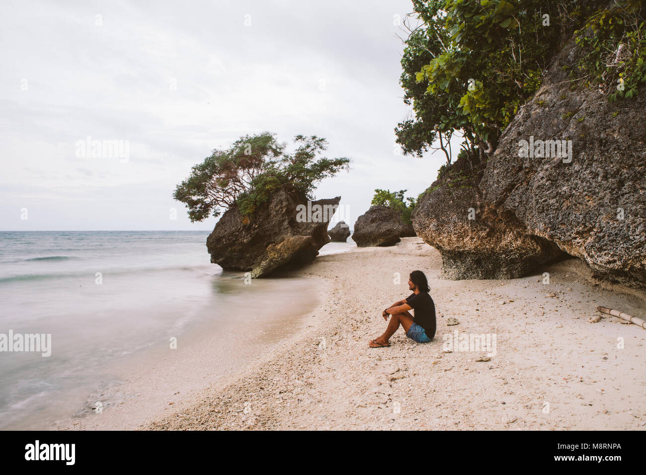 Side view of man sitting against rocks at beach Stock Photo