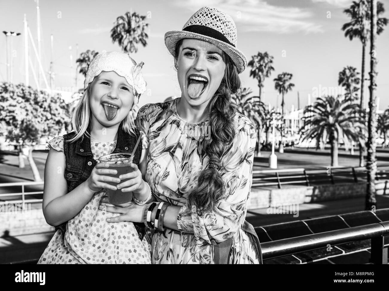 Summertime at colorful Barcelona. happy modern mother and child tourists on embankment in Barcelona, Spain showing tongues after drinking bright red b Stock Photo