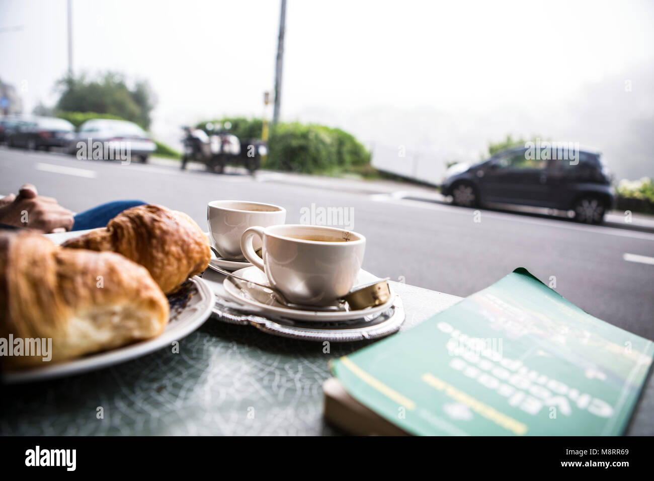 Ein französisches Frühstück auf einem Bistrotisch in der belgischen Kleinstadt Bouillon in Belgien: 2 Tasse Kaffee, ein Korb mit Croissants und ein gr Stock Photo