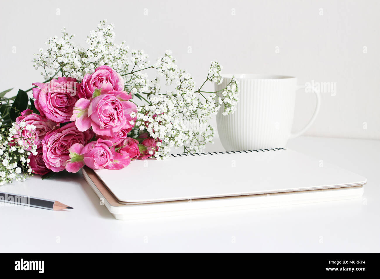Styled stock photo. Closeup of wedding bouquet made of pink roses and baby's breath, Gypsophila flowers lying on white table, feminine still life, bla Stock Photo