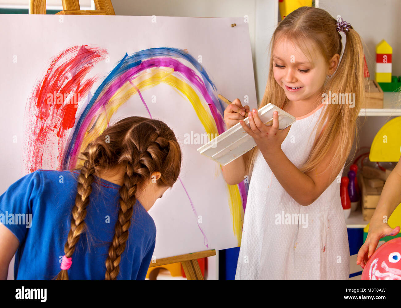 Children painting finger on easel. Group of kids with teacher. Stock Photo