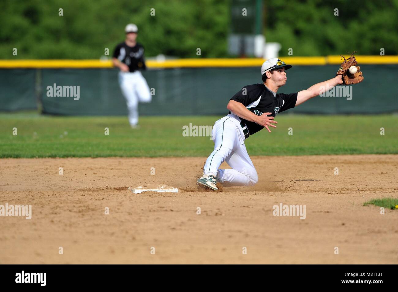 Second baseman lunging to catch a throw from his catcher in an effort