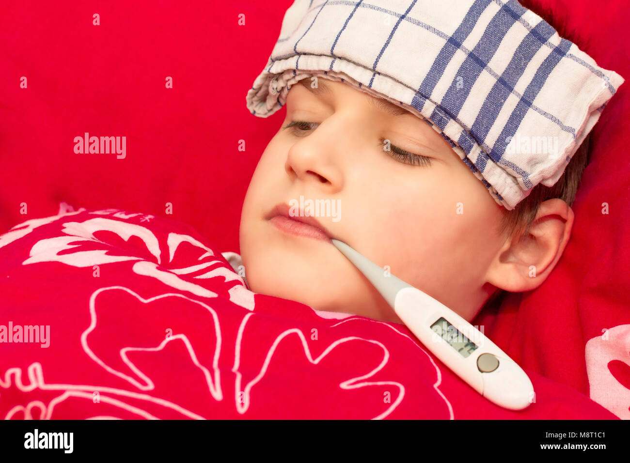 A sick boy lying in bed with a thermometer in his mouth. Cold compress on the forehead of a child. Influenza epidemic in the Czech Republic. Temperatu Stock Photo