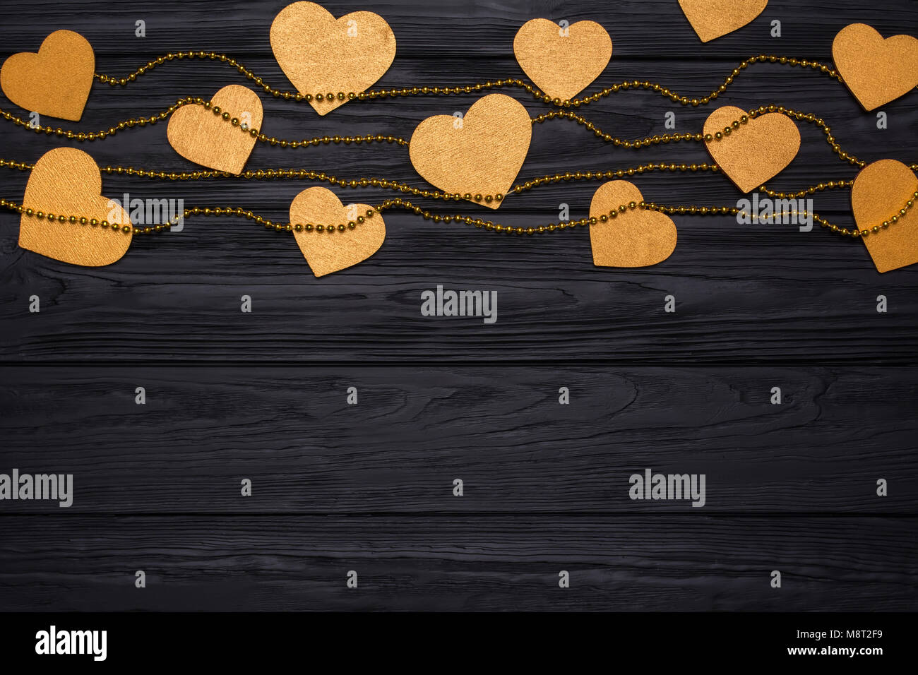 Flat lay border of golden hearts and beads. Festive decor on a black wooden Stock Photo