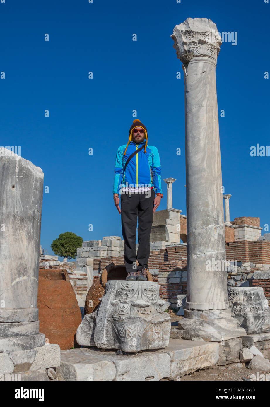 Man in baseball cap NYC is sitting under the arc of The Gate of Augustus in Ephesus was built to honor the Emperor Augustus and his family. Now it is Turkey Stock Photo