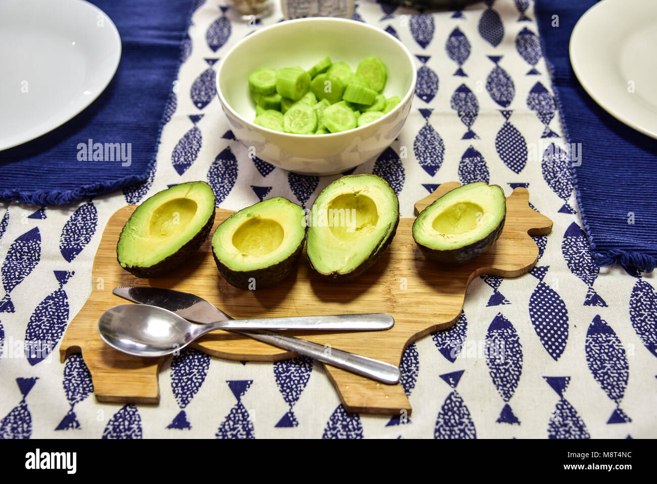 4 halved avocados sit on a cute cow-shaped wooden cutting board. A bowl of  fresh cucumbers sits in background. Dinner at home Stock Photo - Alamy