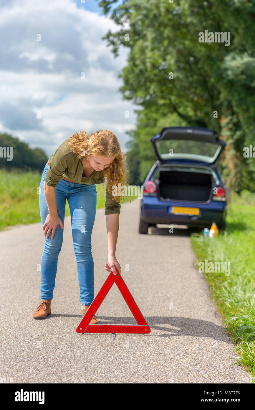 Caucasian teenage girl placing hazard warning triangle on rural road Stock Photo