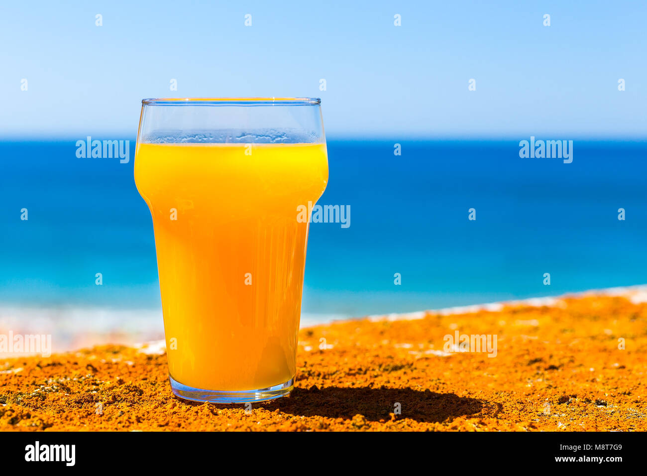 Glass filled with orange juice at blue sea with sky Stock Photo