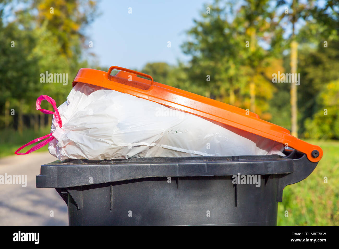 Trash can filled with garbage along street in nature Stock Photo