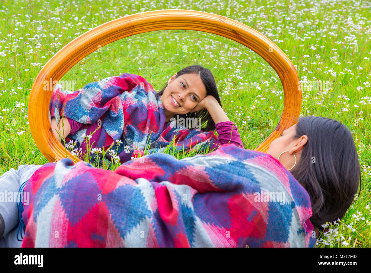 Young colombian woman lying in blooming pasture with mirror Stock Photo