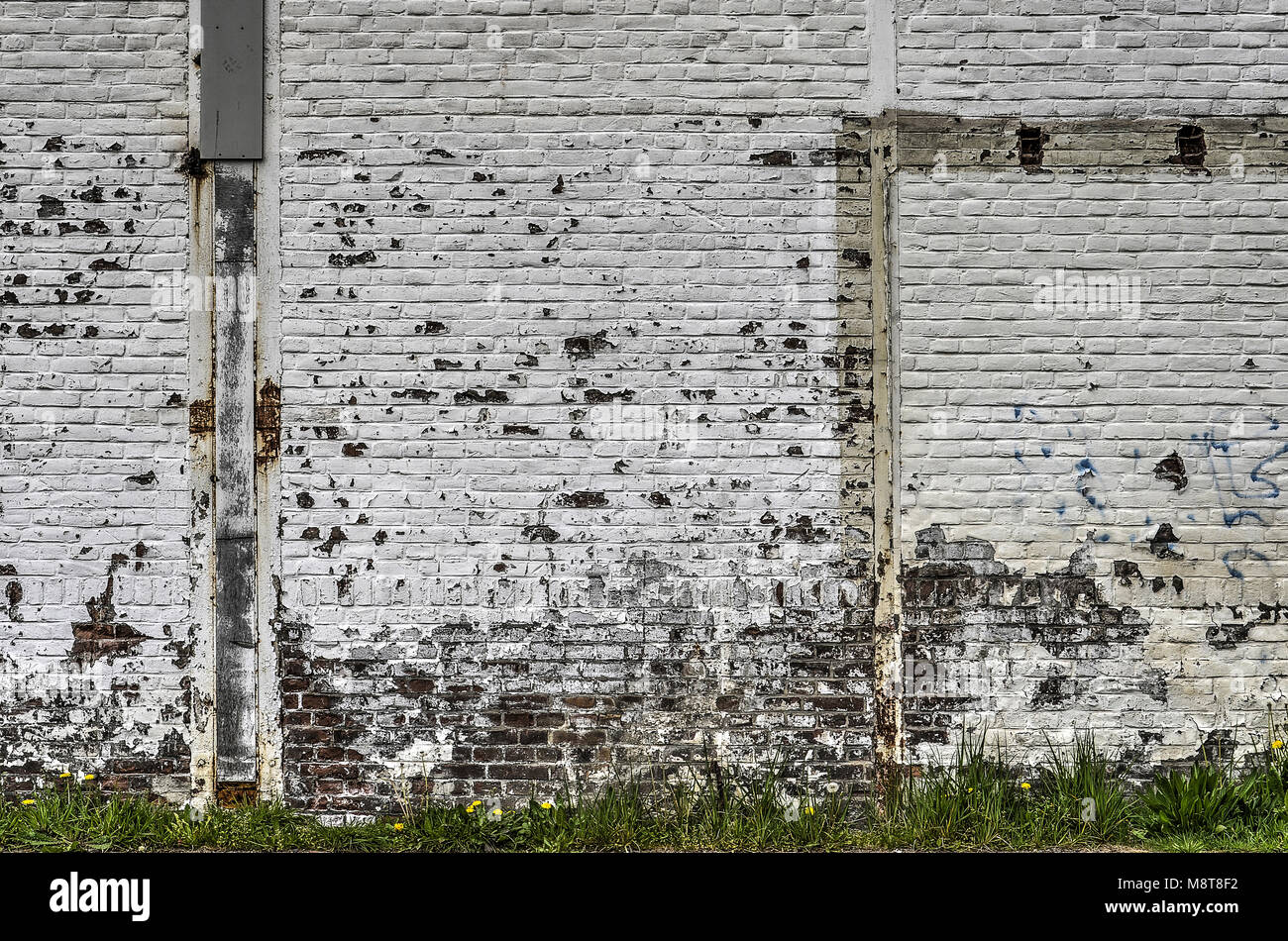 Old brick wall with peeling white paint and remnants of demolished adjacent elements Stock Photo