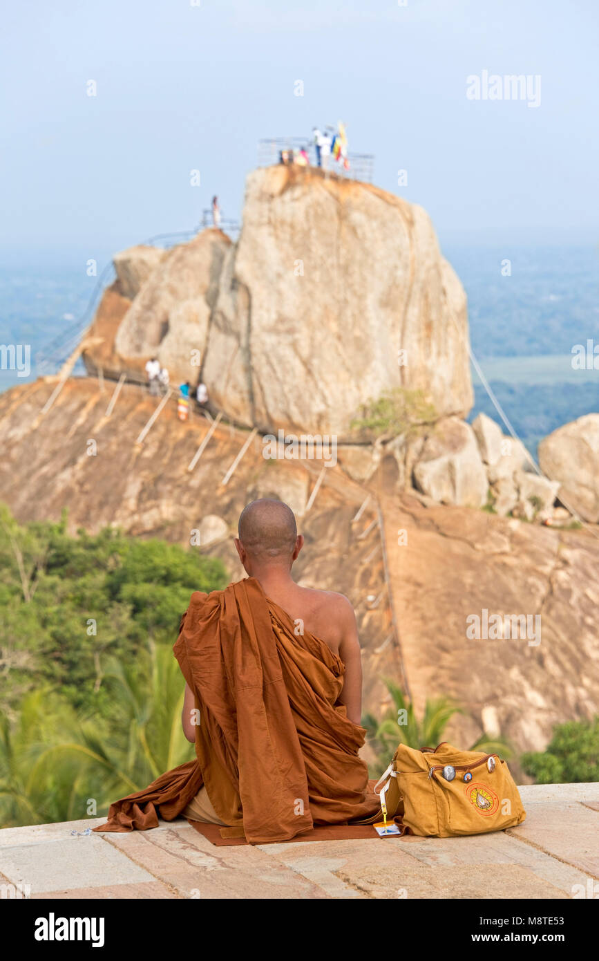 A Buddhist monk sits in contemplation on Mihintale and facing Aradhana Gala which pilgrims and tourists climb to pray or look at the view, Stock Photo