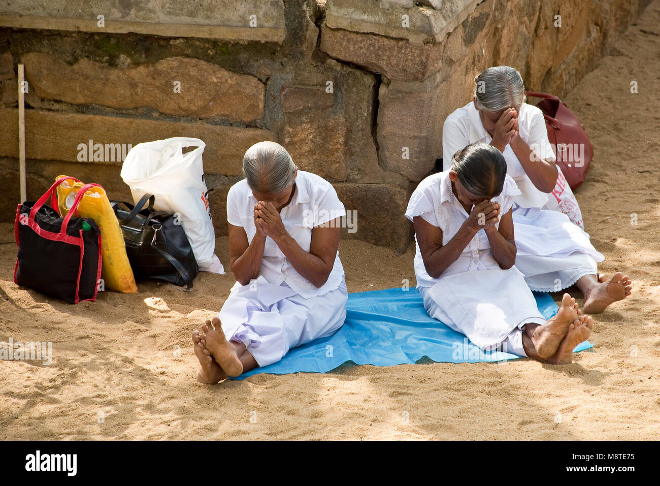3 three elderly Sri Lankan women praying and meditating at the Jaya Sri Maha Bodhi temple in Anuradhapura, Sri Lanka. Stock Photo