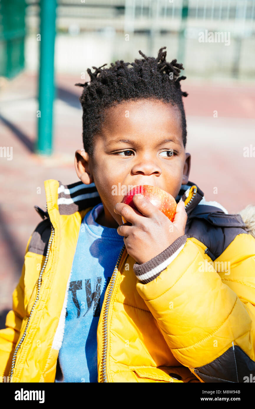 Cute little boy with a yellow coat eating a red apple at the school in a  sunny day Stock Photo - Alamy
