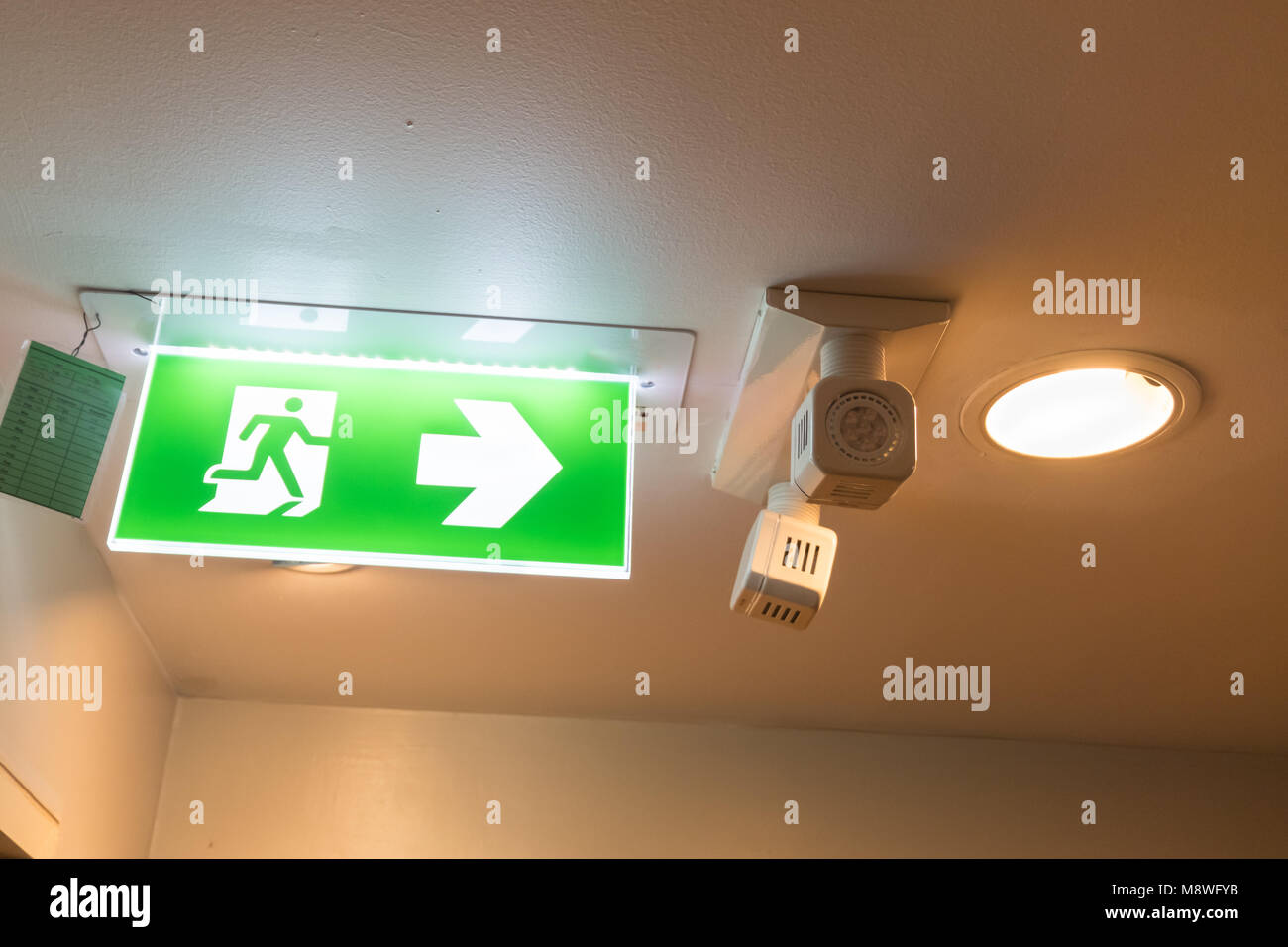 Green emergency exit sign showing the way to escape. Stock Photo
