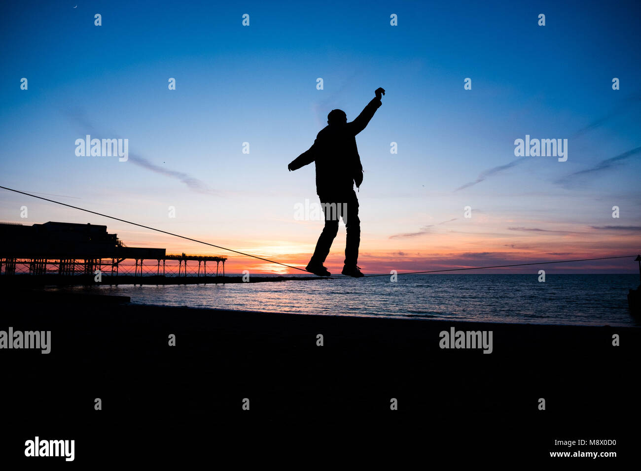 Aberystwyth Wales UK, Tuesday   20 March 2018  UK Weather:   A young man is silhouetted as he practices his ’slack-line’ walking  as the sun sets  gloriously  over Cardigan Bay on cold but clear Spring Equinox evening in Aberystwyth on the west coast of Wales.   With day and night of equal length, the spring equinox today marks the start of ’astronomical spring’     photo © Keith Morris  / Alamy Live News Stock Photo