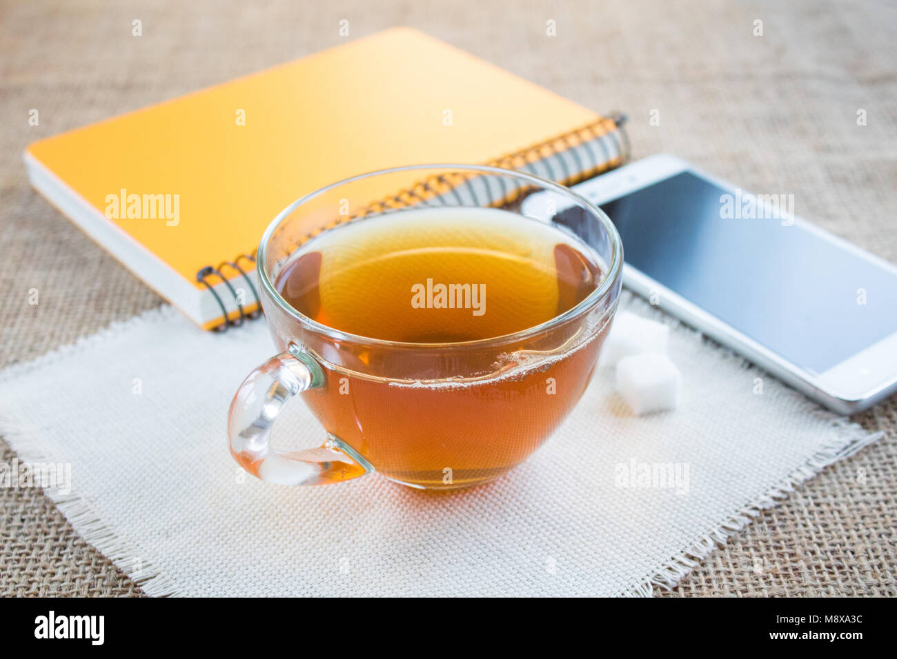 Morning cup of tea. Near the cup is a white smartphone. Notepad to write plans for the day. Stock Photo