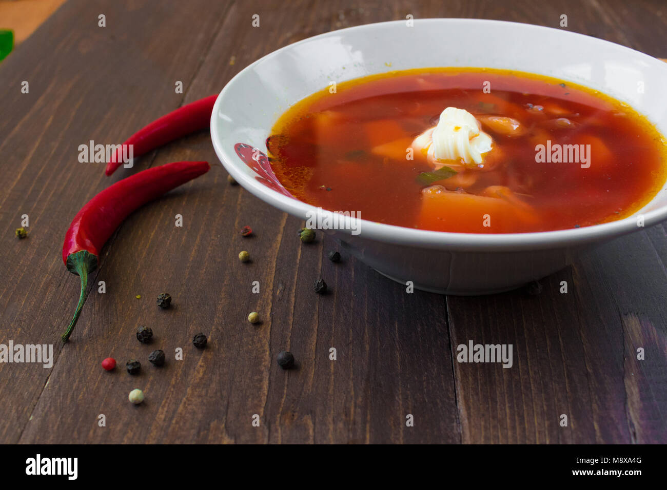 A bowl of borsch with sour cream. Spices and chili pepper are spilled around the plate Stock Photo