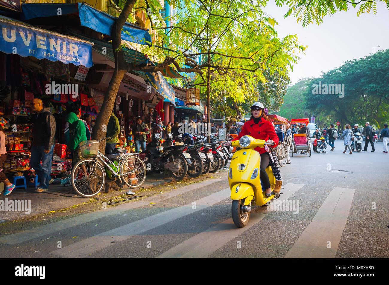 Vietnam scooter, view of a young Vietnamese woman riding a yellow scooter into the Old Quarter in the center of Hanoi, Vietnam. Stock Photo