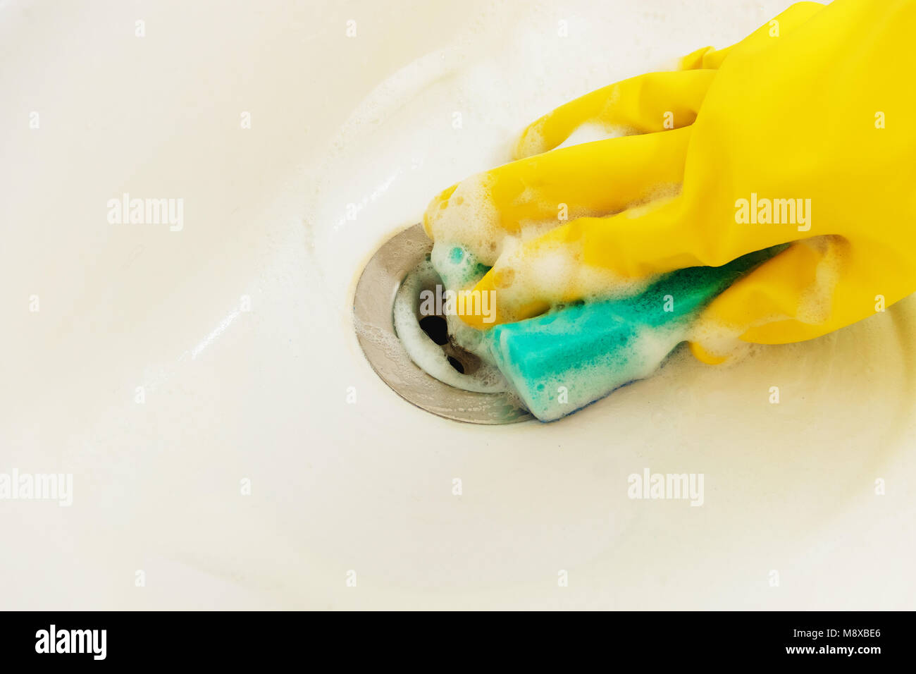 Cleaning Bathroom Sink with Detergent in Yellow Rubber Gloves with Blue Sponge - Housework, Spring Cleaning Concept Stock Photo