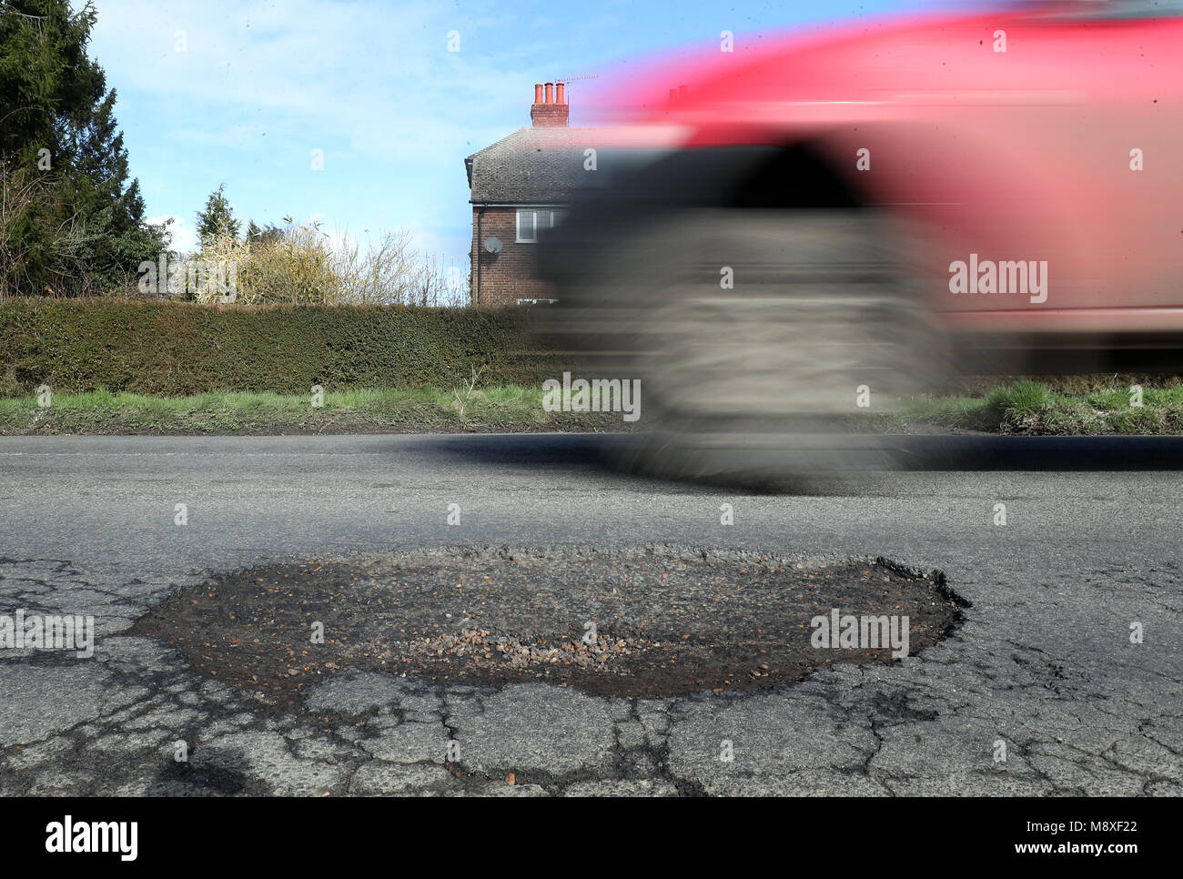 A car passes a large pothole near Ashford in Kent. One in five local roads is in a poor condition as councils face a huge funding deficit to tackle potholes, according to a new report. Stock Photo