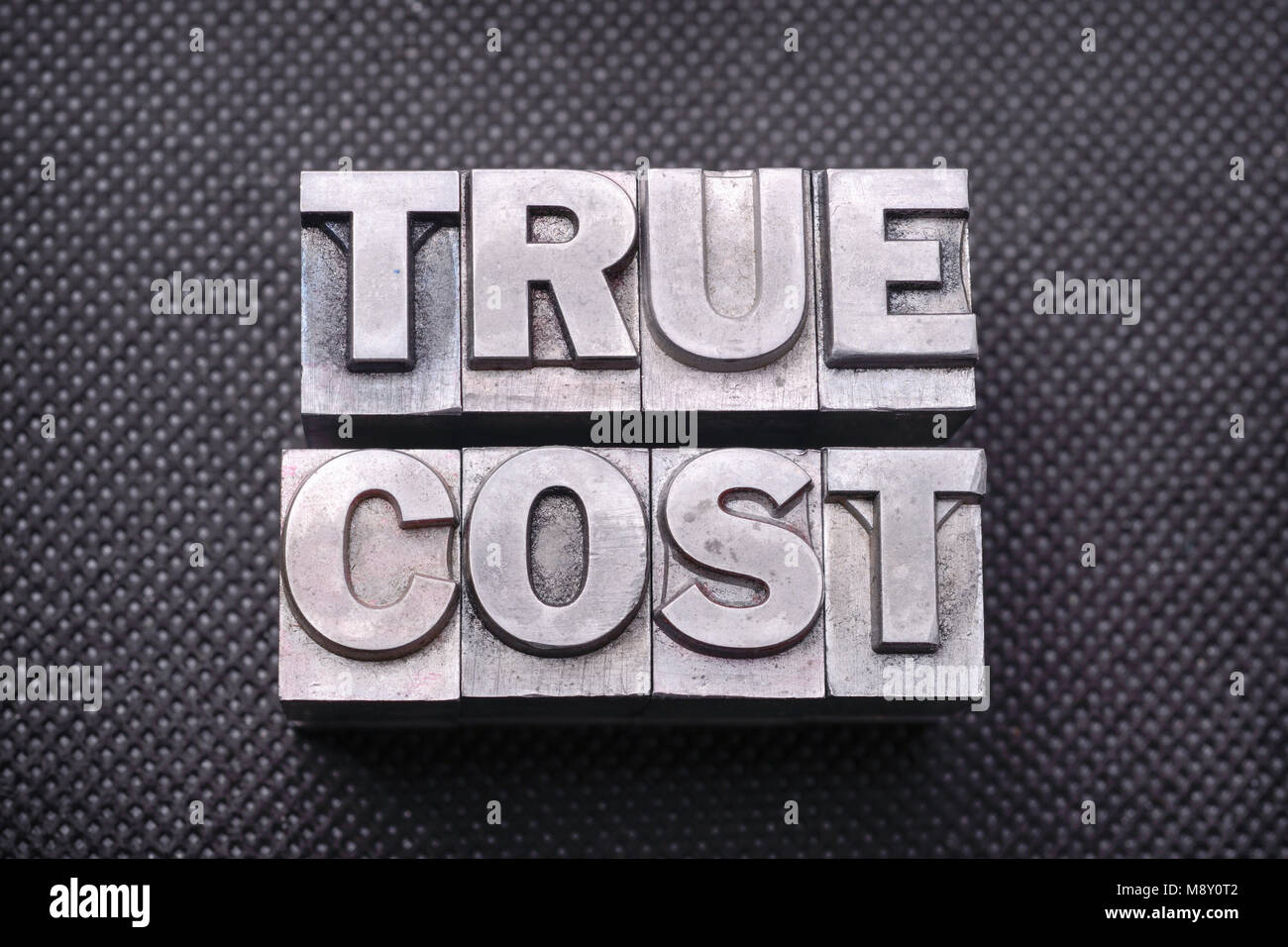 true cost phrase made from metallic letterpress blocks on black perforated surface Stock Photo