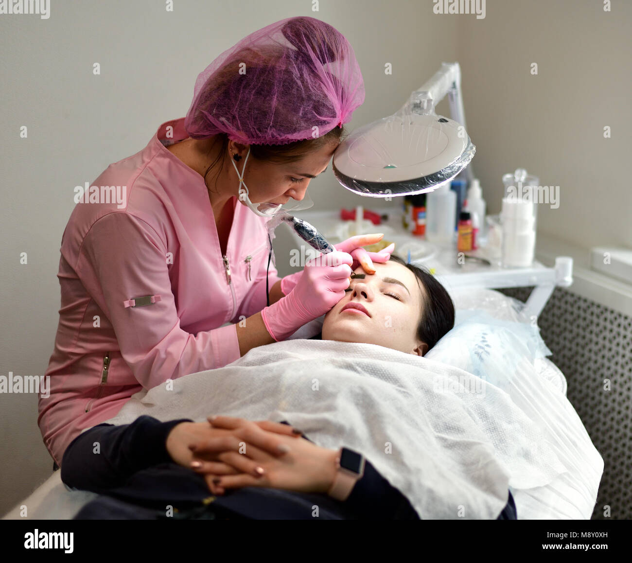 The master makes eyebrow tattoos for a young girl. Stock Photo