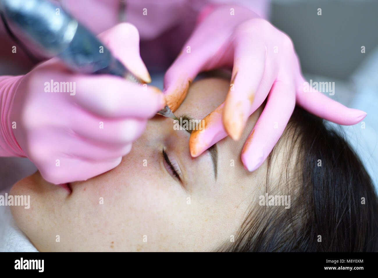 The master makes eyebrow tattoos for a young girl. Stock Photo