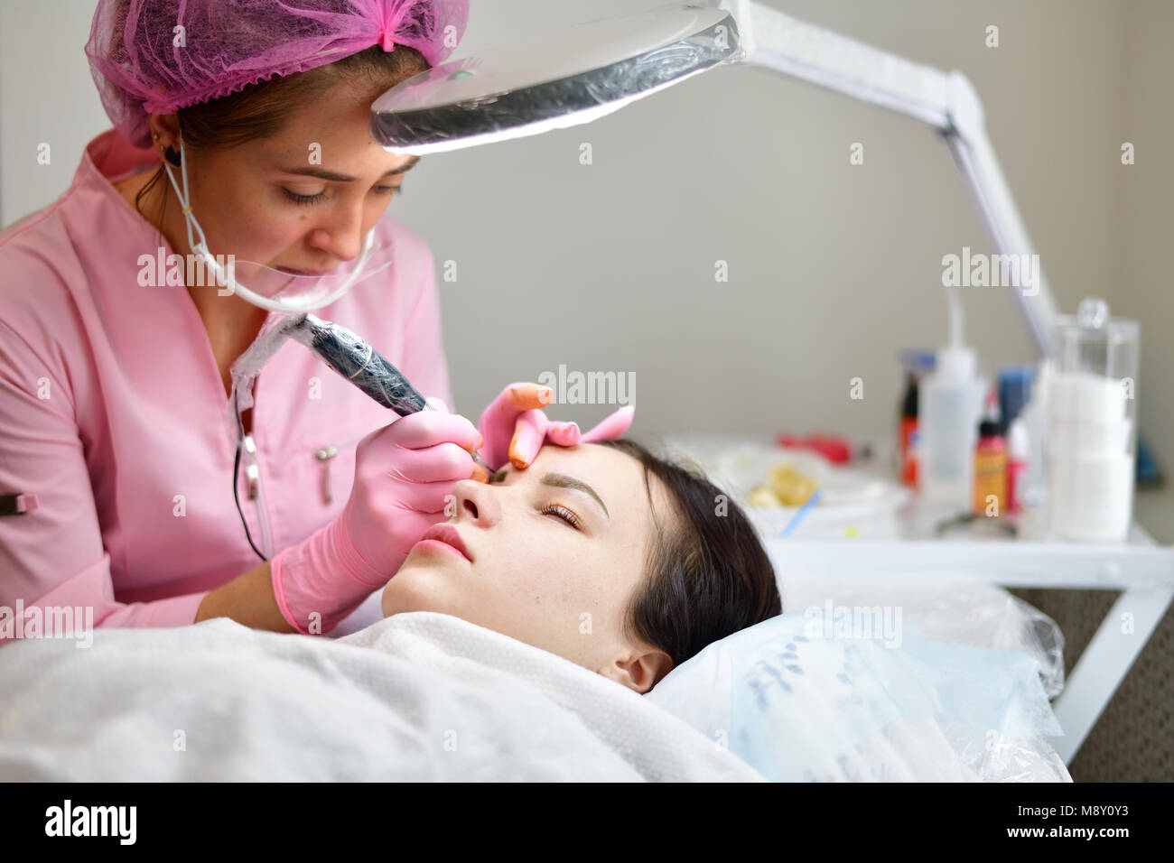 The master makes eyebrow tattoos for a young girl. Stock Photo