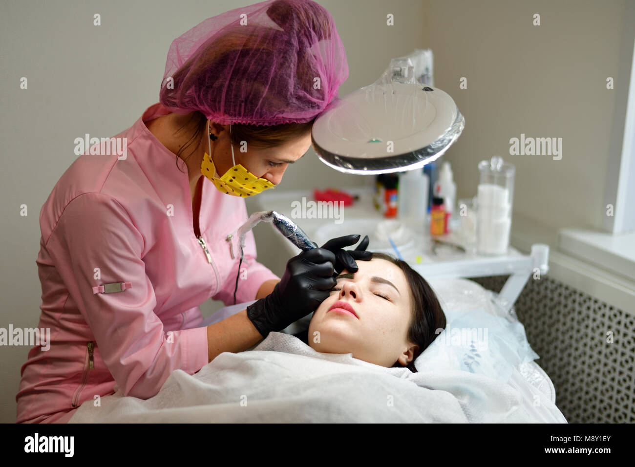 the master does the tattoo on the eyebrows to the girl. Stock Photo