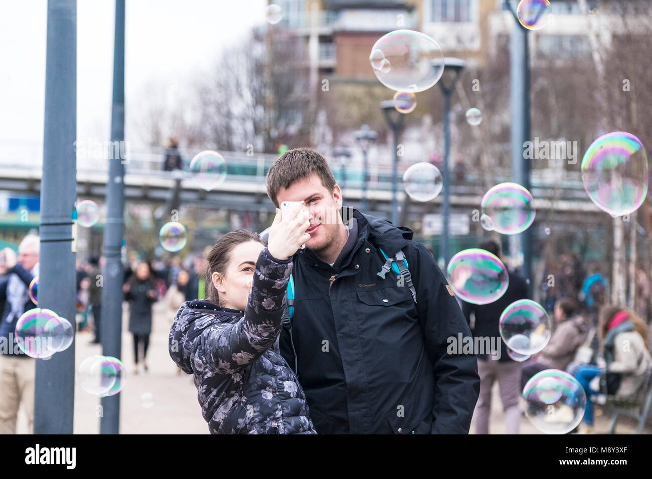 Bubbles floating past a couple as they take a selfie on a smartphone. Stock Photo