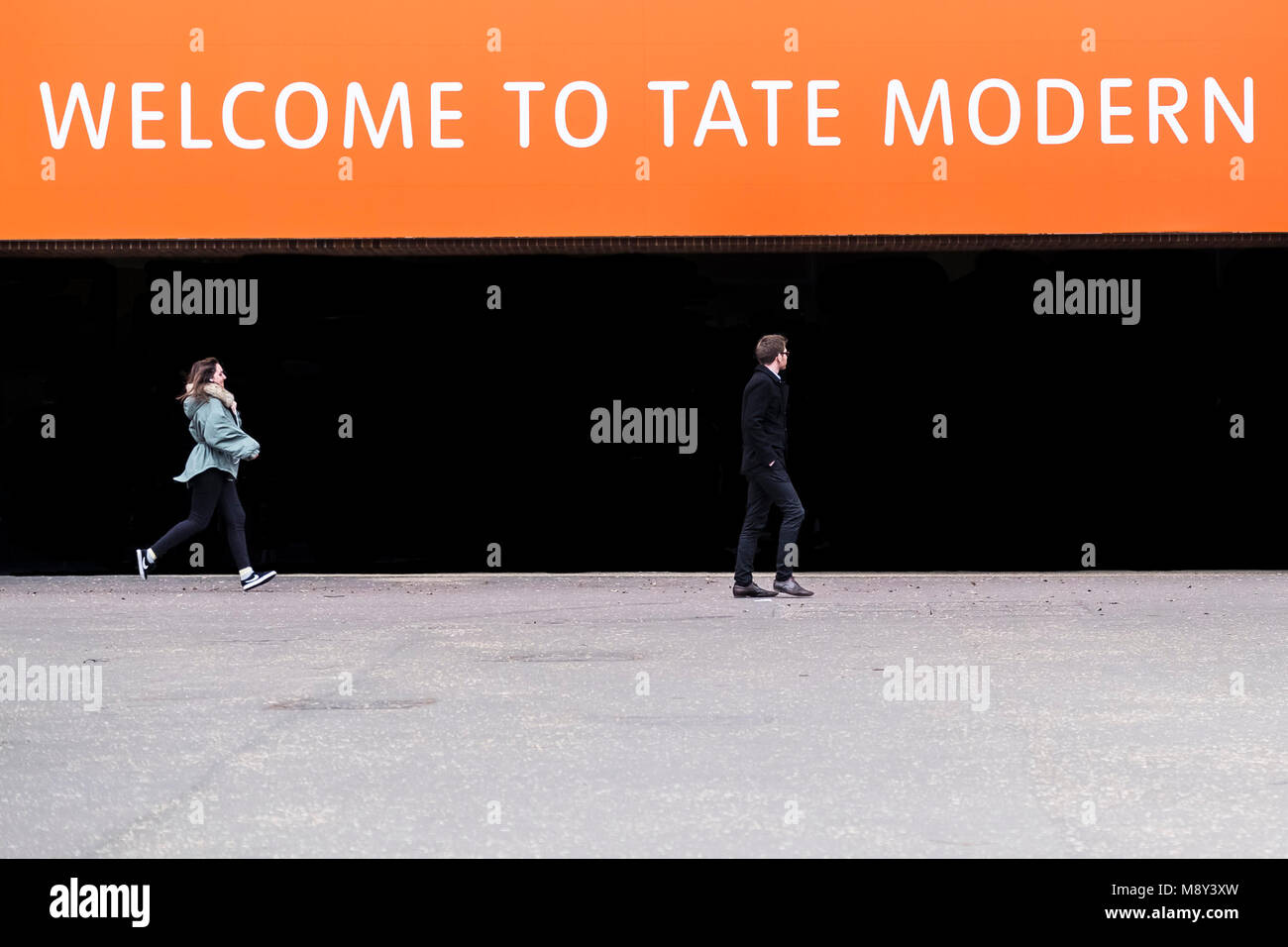A woman running after a man in front of the Entrance to the Tate Modern in London. Stock Photo