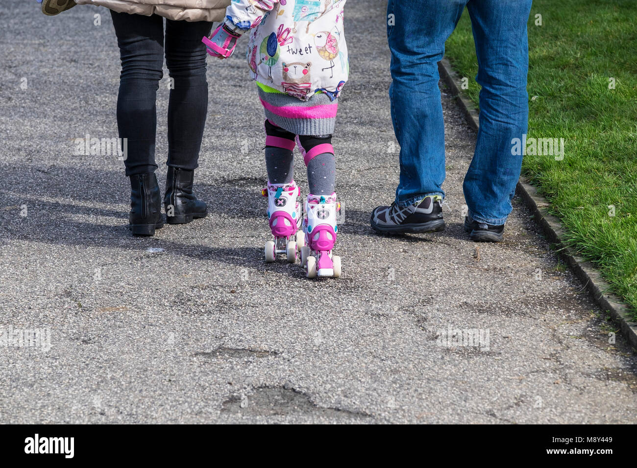 Two adults walking either side of a child wearing roller skates. Stock Photo