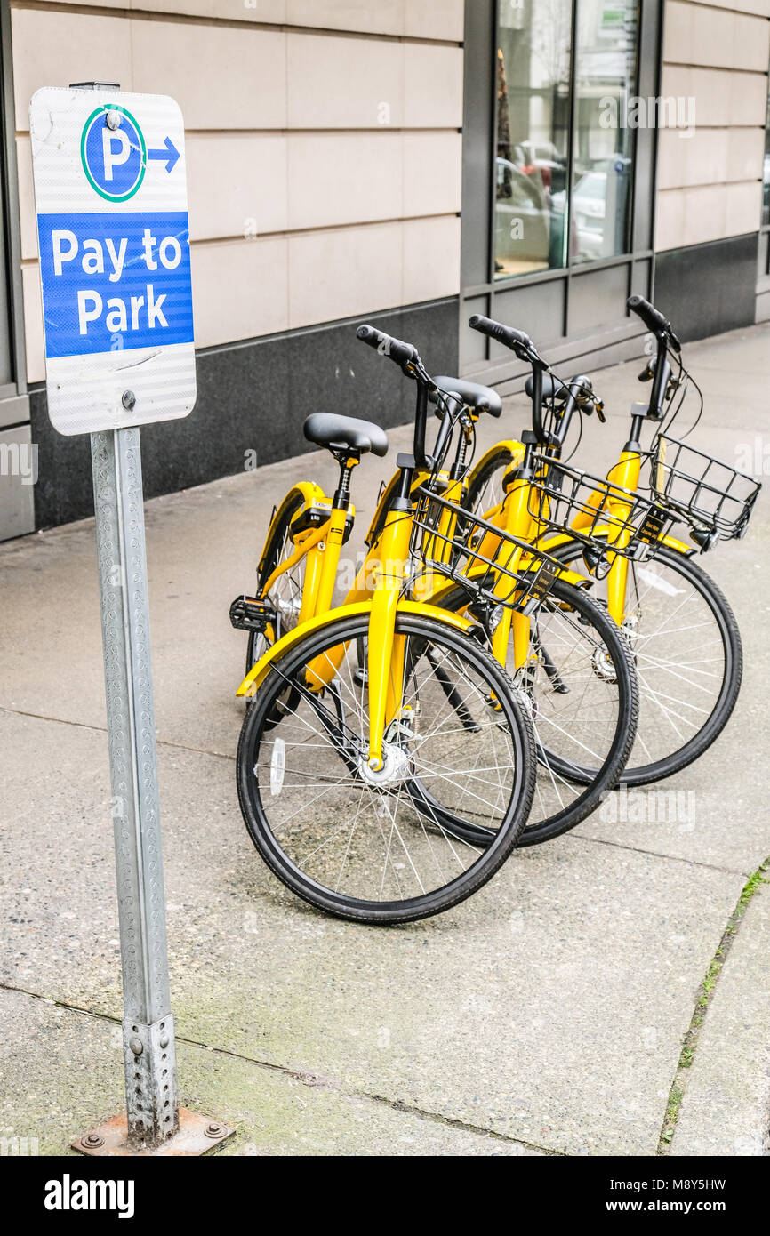 Three yellow Ofo shared dockless bikes by a Pay to Park sign Stock Photo
