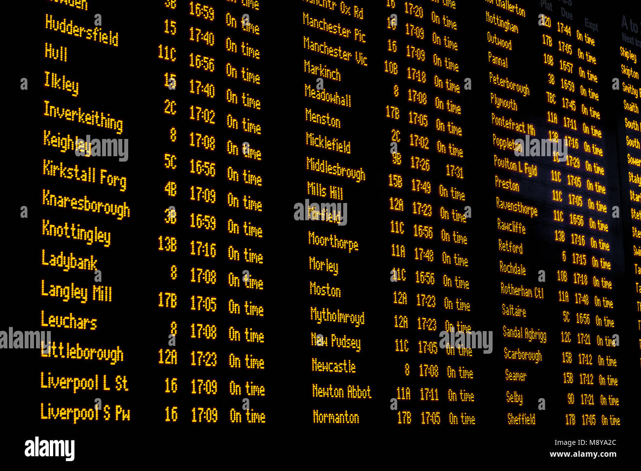 An electronic passenger information board inside a busy train station giving passengers information about destinations, departures, arrivals, delays,  Stock Photo