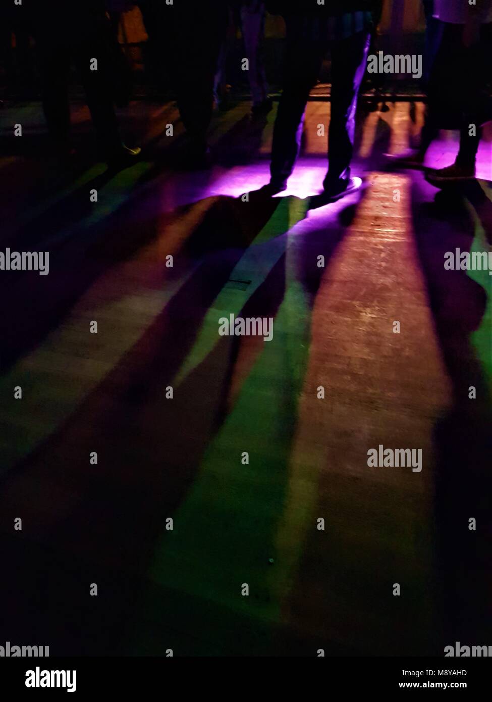 Low view of people standing watching a band at a gig with stage lights making silhouette patterns on wooden floor Stock Photo