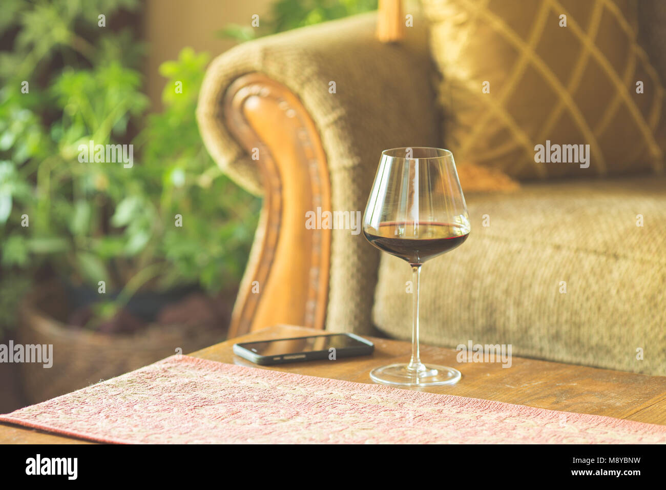 A glass of red wine on the coffee table next to a smart phone Stock Photo